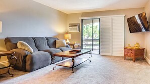 A living room with a sofa, coffee table, lamp, TV, and a sliding glass door. - Lake Access & Community Pool: Cozy Condo in Mound (Mound)