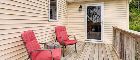 A wooden deck with two red chairs and a small round table.