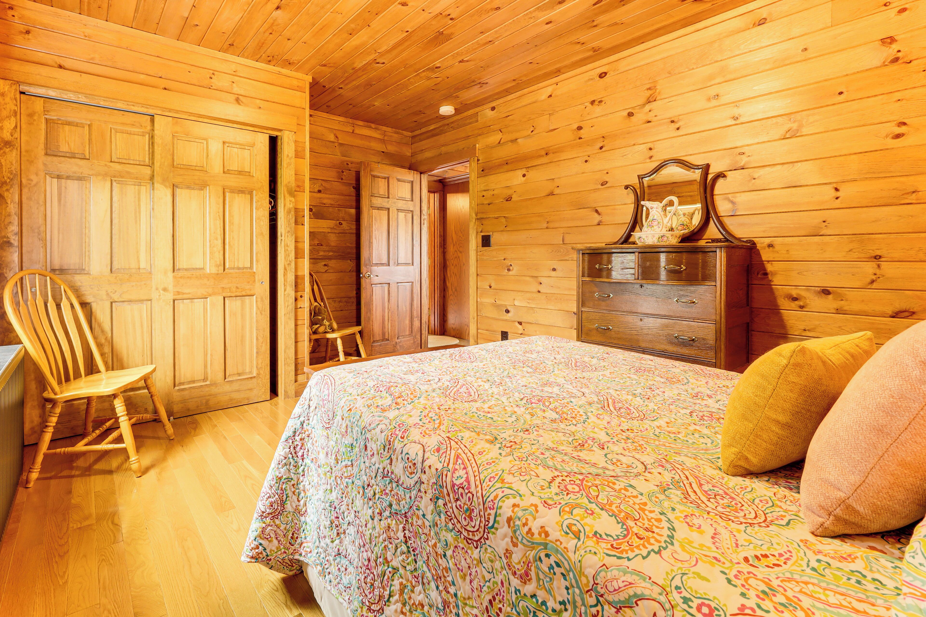 Un dormitorio de cabaña de madera con cama, cómoda y dos sillas.