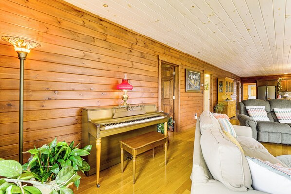 A cozy room with a wooden interior, featuring a piano, a sofa, and a lamp. - The Hideaway in Downeast Maine: Walk to Ocean (Jonesport)