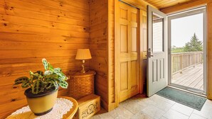 Interior de uma cabana de madeira com uma planta em vaso, uma luminária e uma porta que dá para um deck.