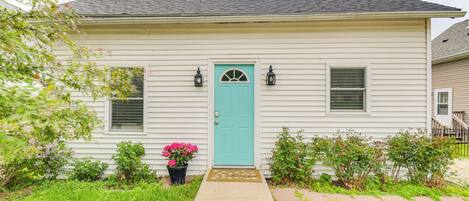 A single-story house with a teal front door, two windows with shutters, and a small porch area.