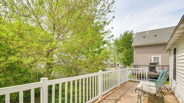 A wooden deck with a white railing, a rocking chair, and a house in the background.