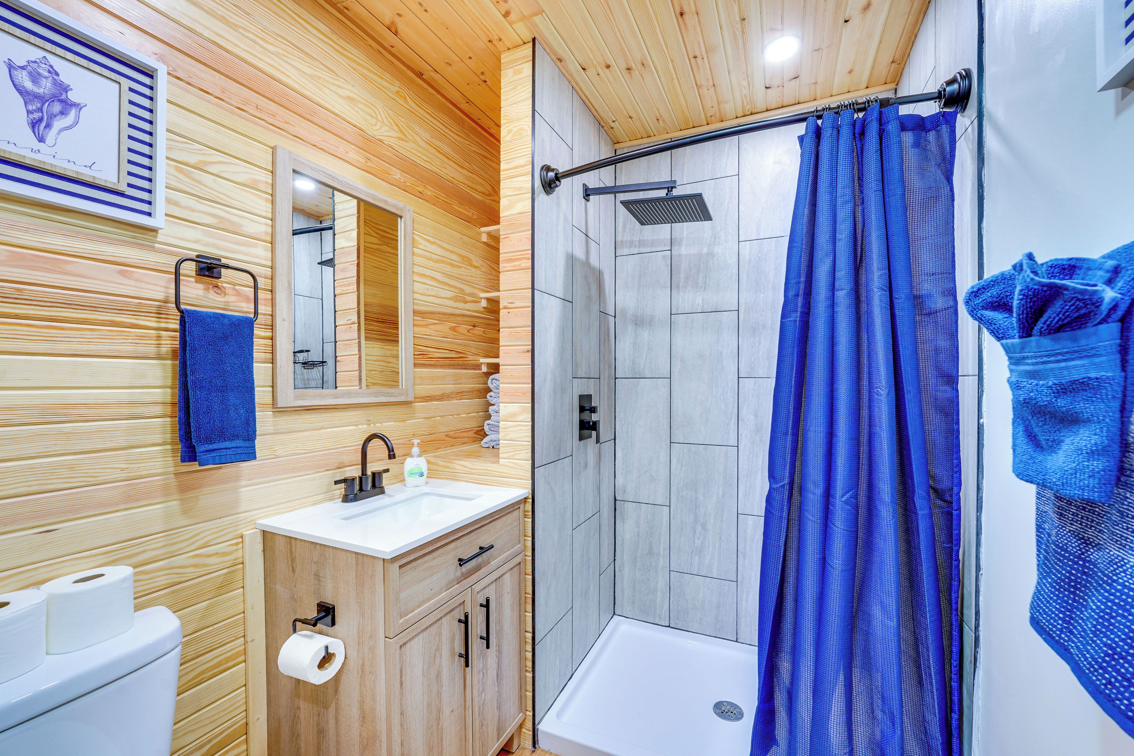Une salle de bain aux murs lambrissés, équipée d’une douche, d’un lavabo et de toilettes.