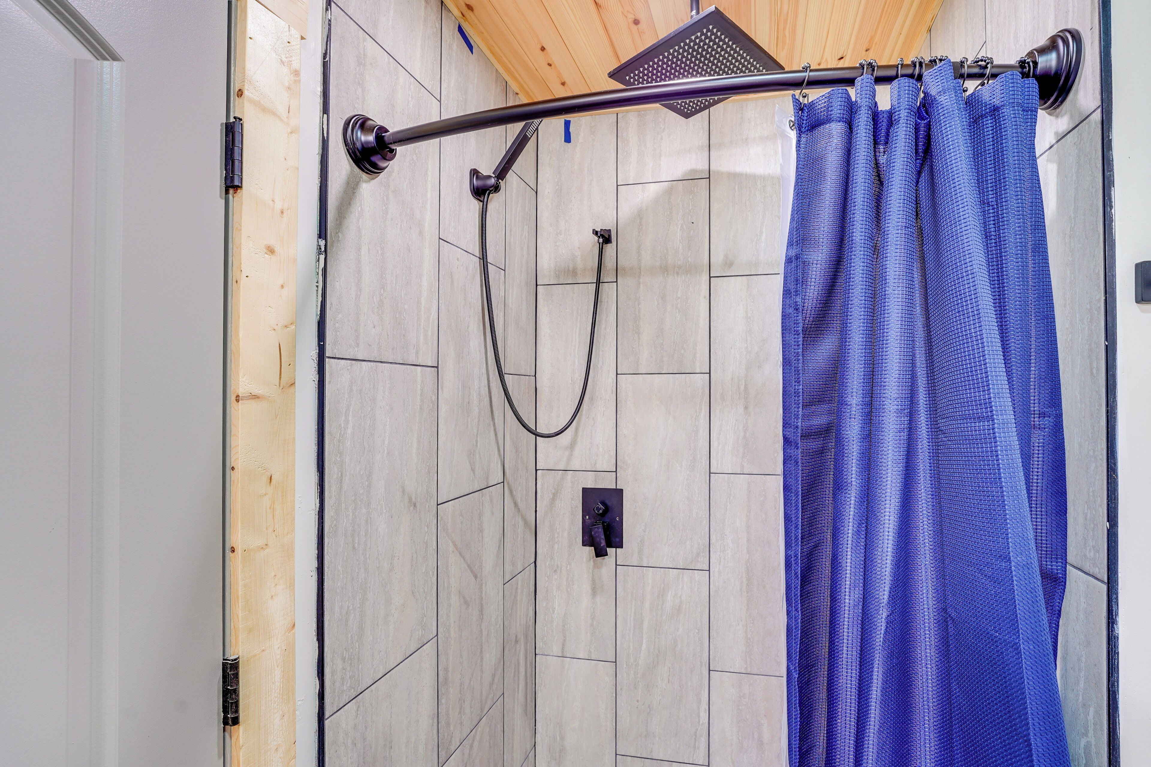 A shower area with a wooden ceiling, tiled walls, and a blue shower curtain.