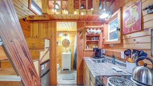 A rustic kitchen with wooden walls, a sink, stove, and various kitchen utensils. - Tiny Home w/ Private Sauna in Woods of Newport! (Newport)