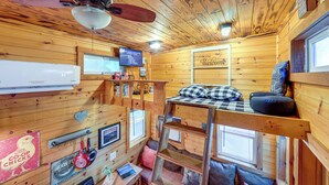 A cozy cabin interior with a bunk bed, wooden walls, a ceiling fan, a mounted TV, and a welcome sign. - Tiny Home w/ Private Sauna in Woods of Newport! (Newport)