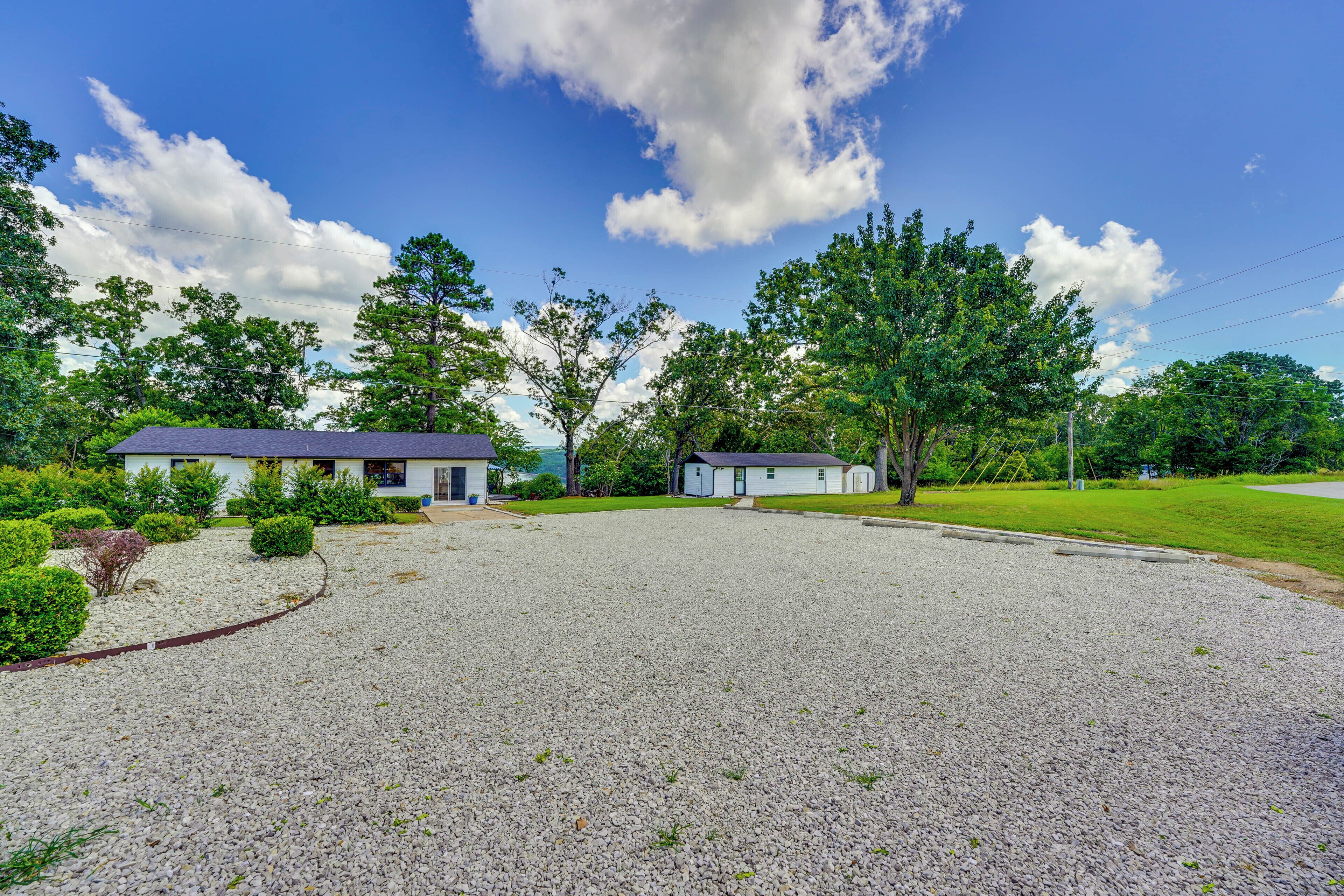 A residential area with a gravel driveway, a small house with a blue roof, and a white building with a dark roof.