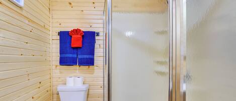 A small, wooden-paneled bathroom with a toilet, a blue towel, and a glass shower enclosure.
