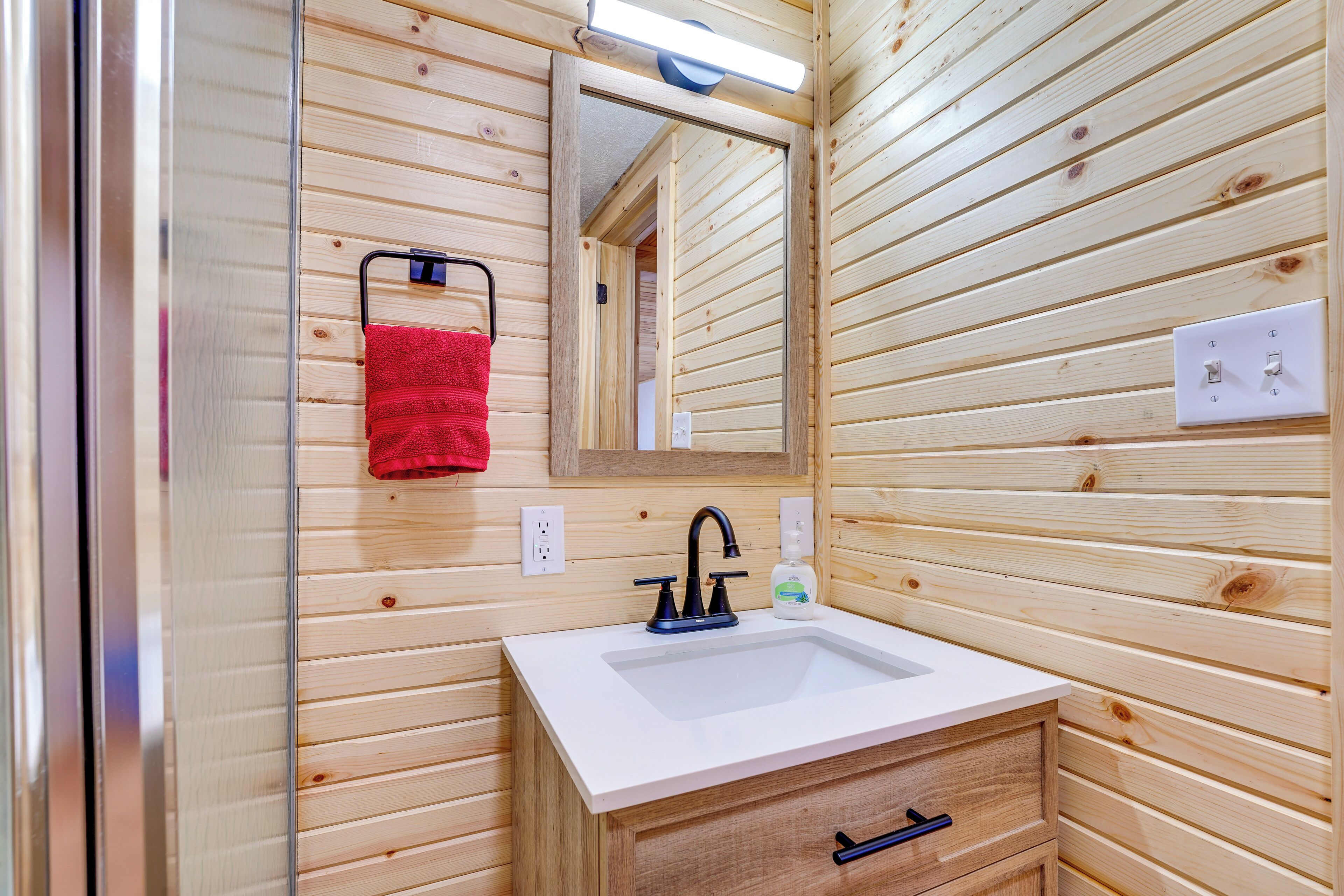 Een badkamer met houten lambrisering, een witte wastafel, een spiegel en een rode handdoek aan een rek.