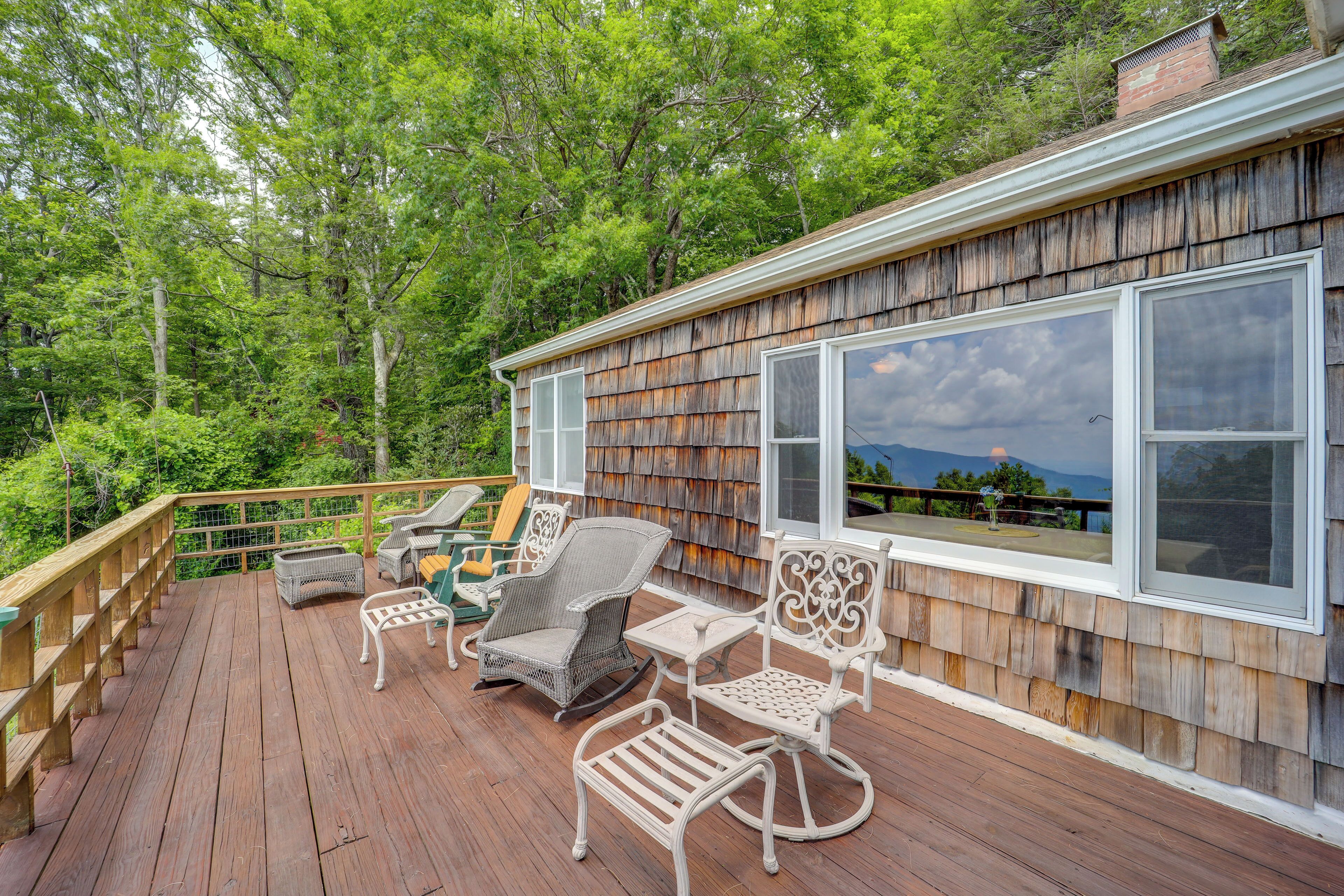 A wooden deck with outdoor furniture, a railing, and a view of a forested area.