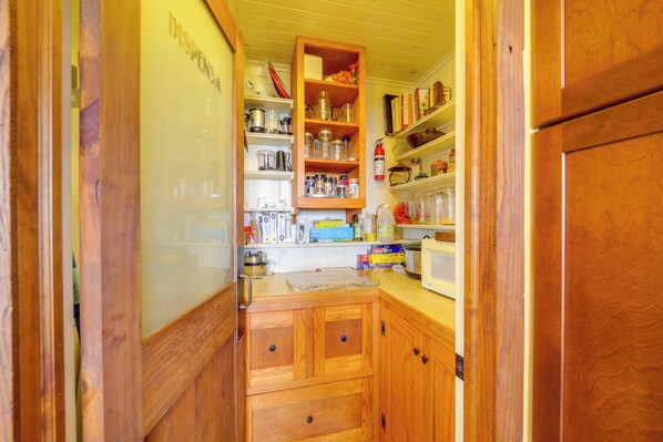 A compact kitchen with wooden cabinets, a microwave, and various kitchen items on shelves.
