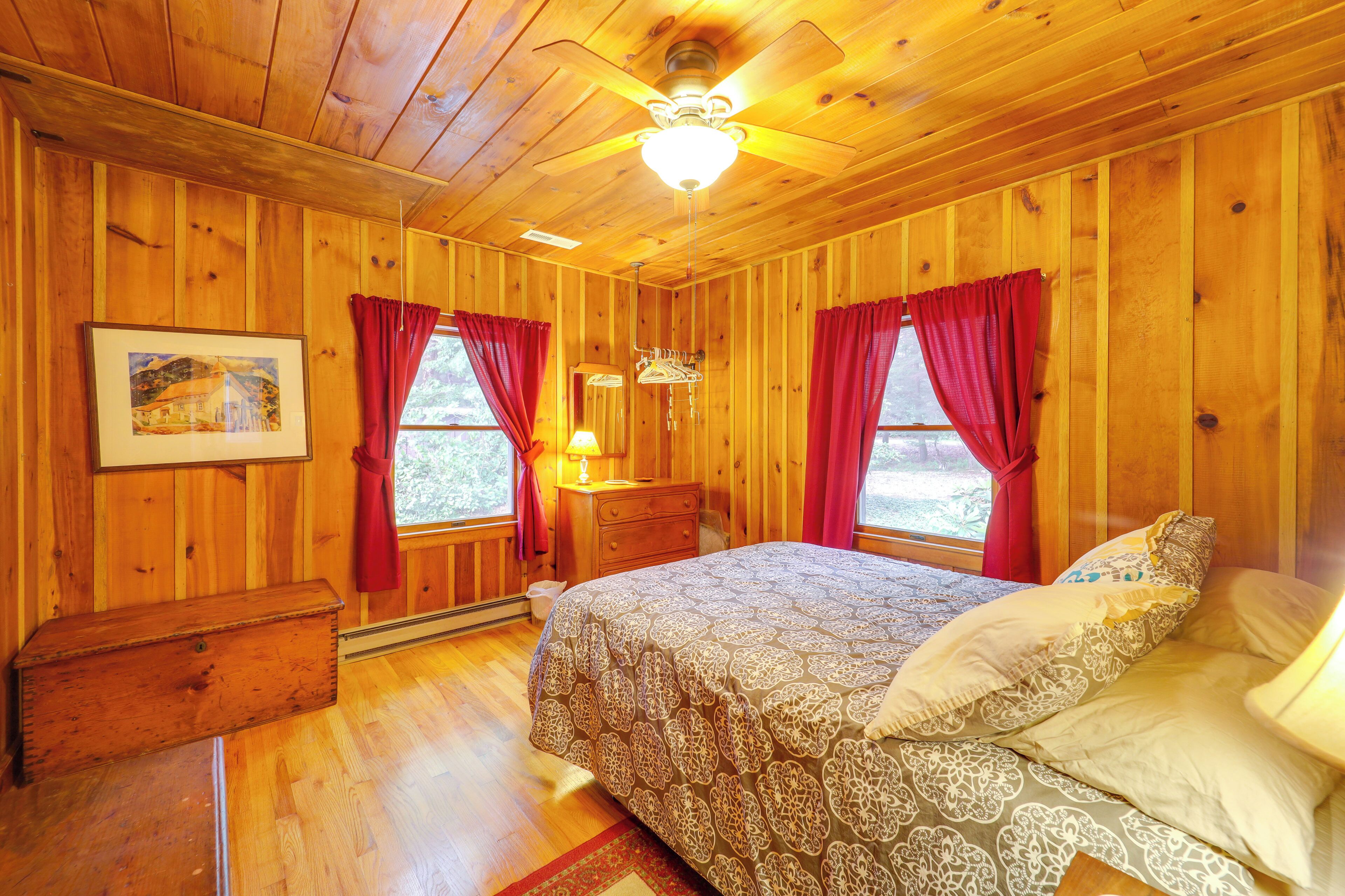 A wooden cabin bedroom with a bed, a nightstand, a dresser, and a ceiling fan.