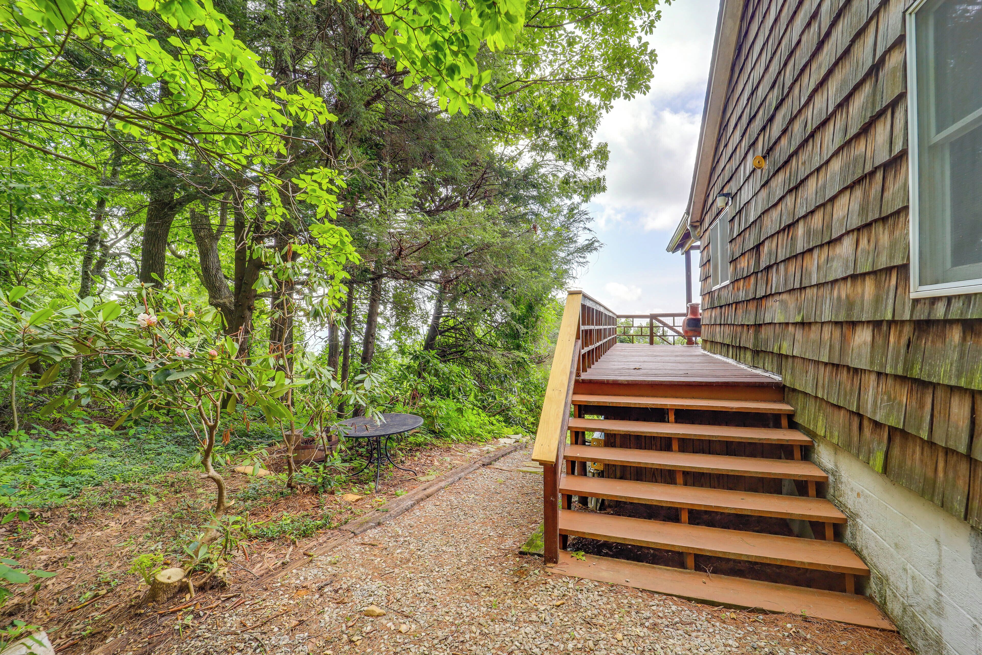 A wooden staircase leading to a house with a gravel path and a table with chairs in a wooded area.