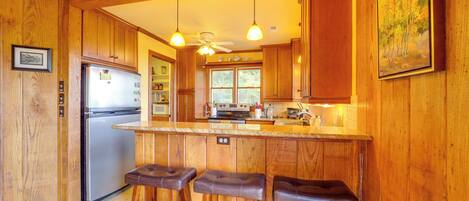 A kitchen with wooden cabinets, a refrigerator, a stove, and three bar stools.