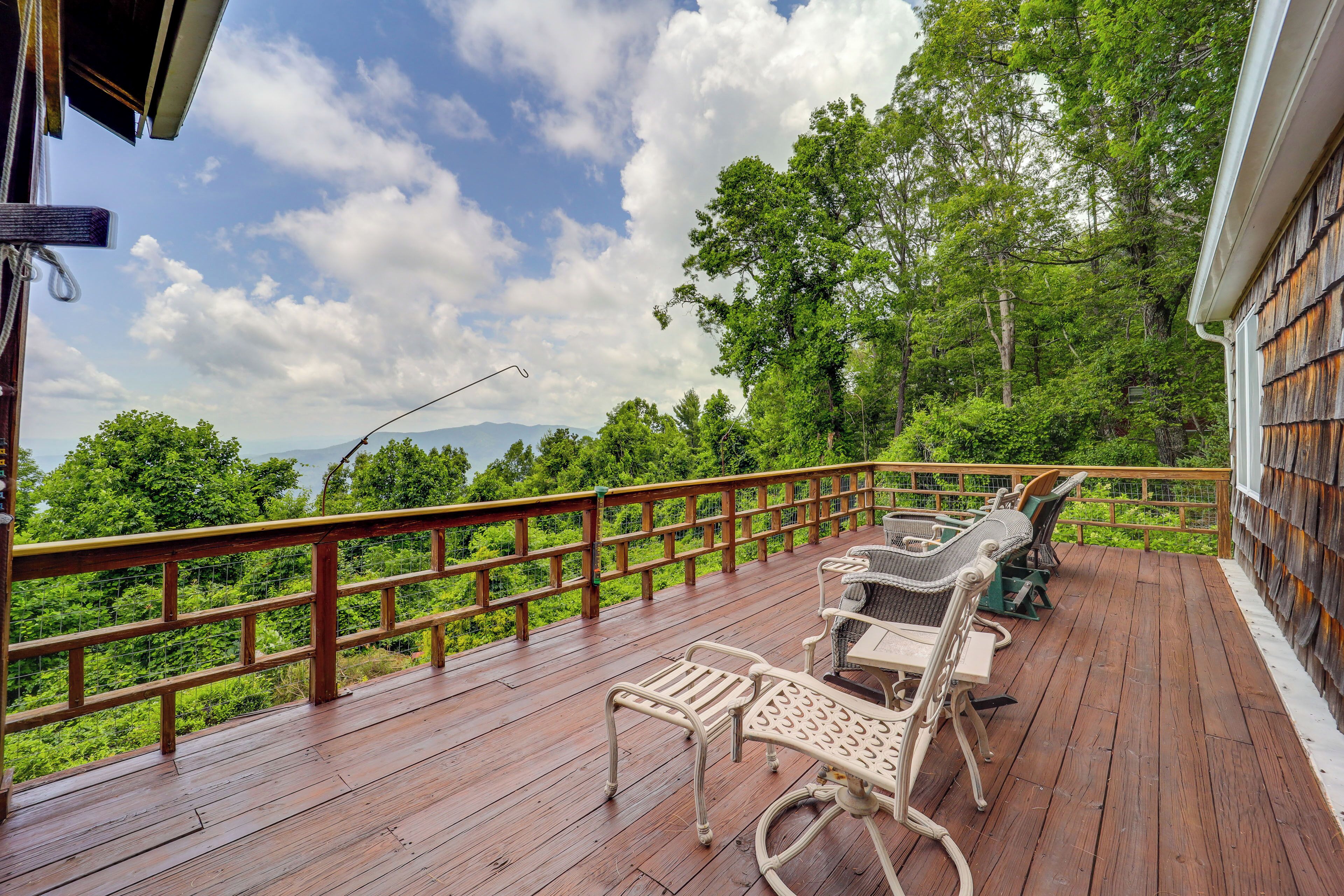 A wooden deck with outdoor furniture and a view of lush greenery and mountains.