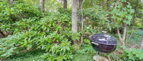 A forest with a black barbecue grill on a stand.