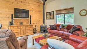 A cozy living room with a wooden wall, a fireplace, a television, and a leather sofa. - Game Room & Deck: Pet-friendly Camp Connell Cabin (Arnold)