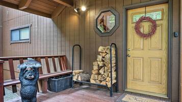 A wooden exterior with a welcome bear sculpture, a door with a wreath, and a stack of firewood.