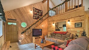 A cozy cabin interior with a wooden staircase, a living area with a couch and a television, and a sign on the door. - Game Room & Deck: Pet-friendly Camp Connell Cabin (Arnold)