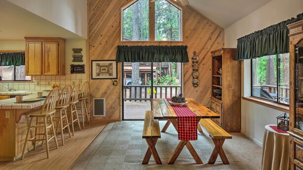 A rustic kitchen with wooden walls, a large window, and a dining area with wooden stools and benches. - Game Room & Deck: Pet-friendly Camp Connell Cabin (Arnold)