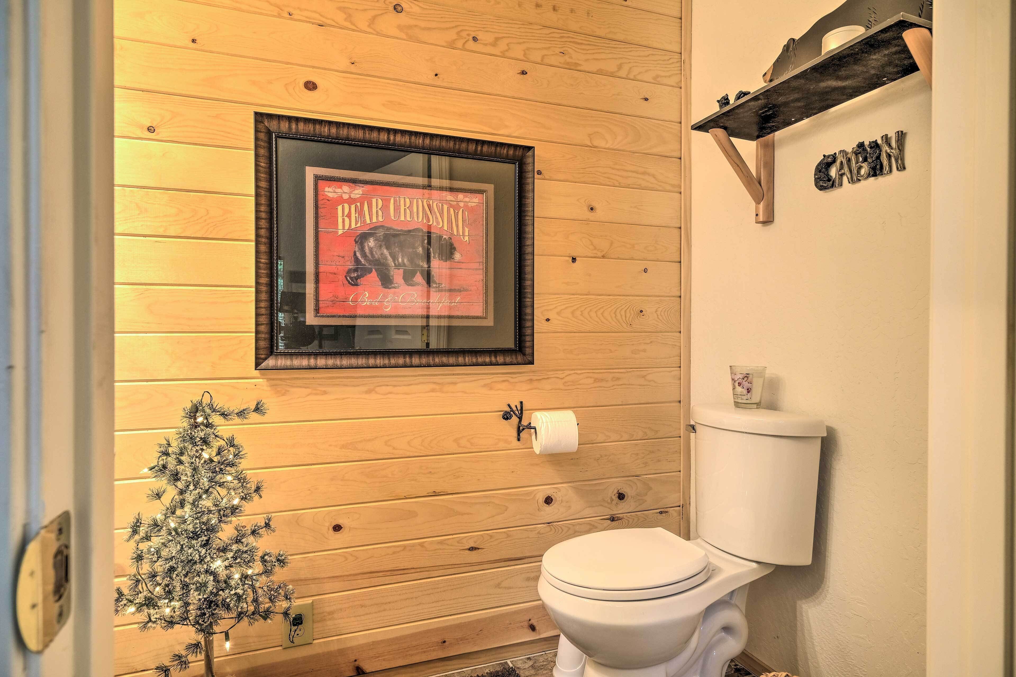 Baño de cabaña de madera con un cartel que indica paso de osos enmarcado, un pequeño árbol de Navidad y un inodoro.