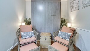 Une pièce comprenant deux fauteuils en osier avec des coussins, une petite commode en bois et un meuble fixé au mur.