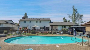 Un jardin avec une piscine, des chaises longues et un patio couvert.