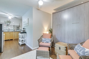 Un salon avec des meubles en osier, une cuisine à l’arrière-plan et une grande armoire.