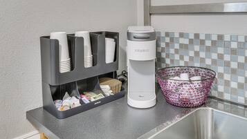 A kitchen counter with a coffee maker, a cup holder with disposable cups, and a basket with cups.