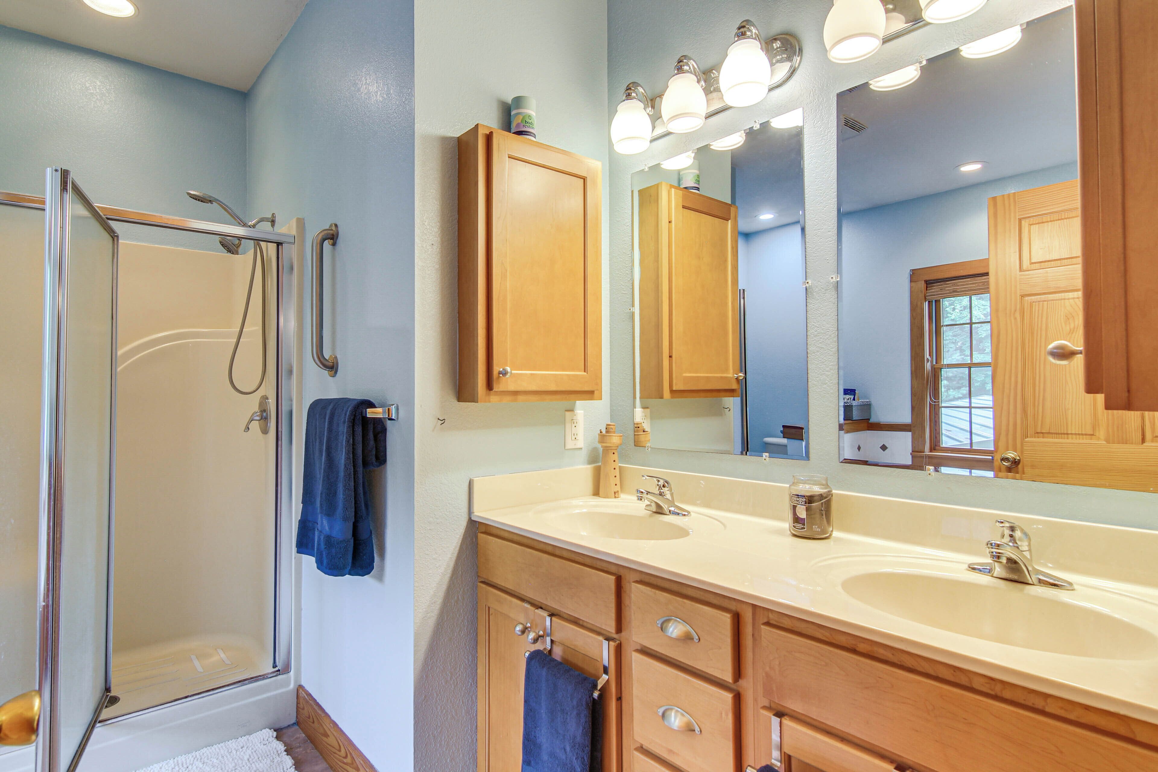 A bathroom with a glass shower enclosure, wooden cabinets, a large mirror, and dual sinks.