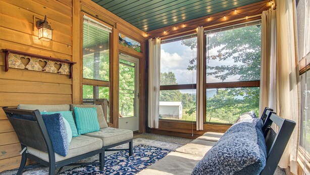 A cozy room with a sofa, a chair, and a window with curtains. - Wraparound Porch w/ Views: Blue Ridge Mtn Gem! (Bakersville)