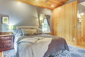 Une chambre avec un grand lit, des murs en bois, une commode et une fenêtre avec des rideaux.
