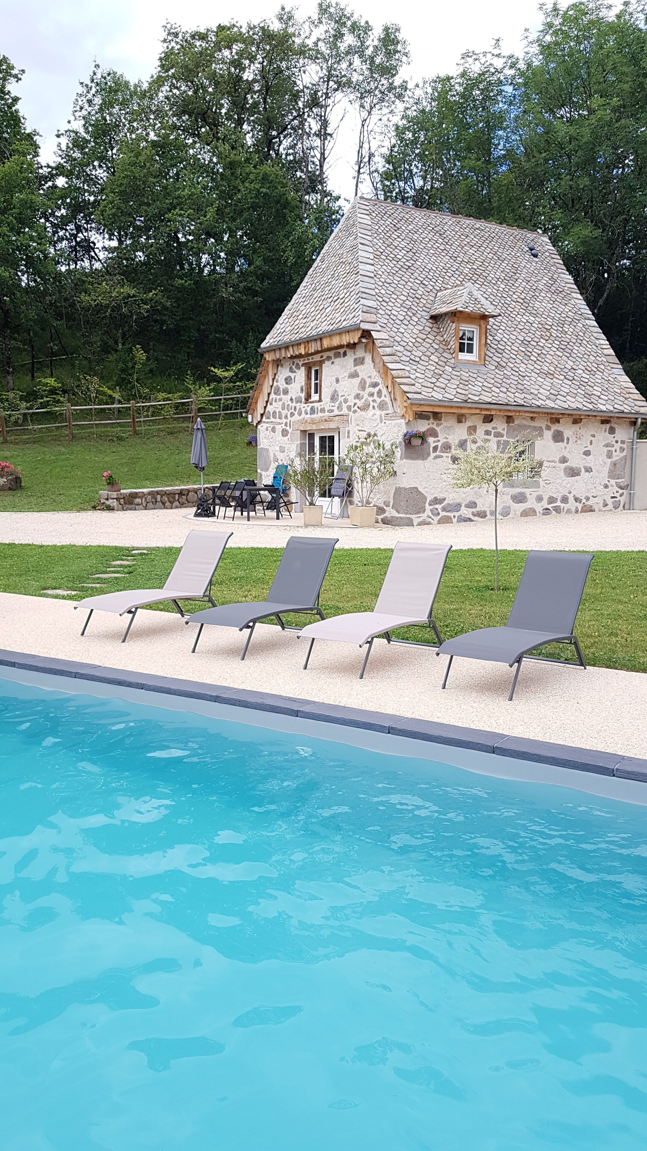Ein Haus aus Stein mit Ziegeldach, einem Swimmingpool und vier Liegestühlen.