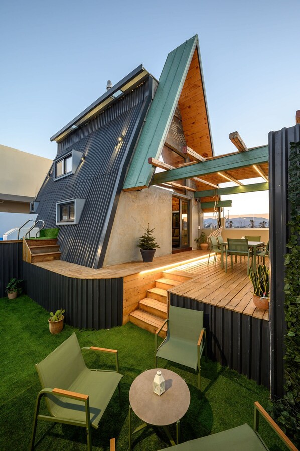 A modern house with a sloped roof, a wooden deck, and outdoor seating.