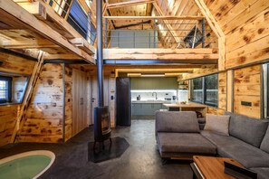 A cabin with a loft bedroom, a kitchen, a living area with a sofa, and a wood-burning stove.