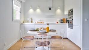 A modern kitchen with white cabinets, a dining table with four chairs, and a window providing natural light. - Le Riviera - Port Cergy | Modern & Cosy (Port-Cergy)