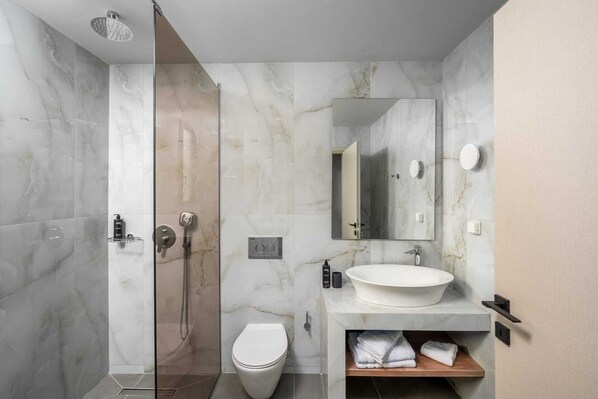 Une salle de bain moderne avec une douche à parois de verre, des toilettes, un lavabo doté d’un plan de travail en marbre et un miroir.