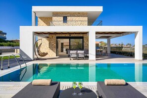 Une maison moderne dotée d’une piscine, d’un espace salon extérieur et d’une façade en pierre.