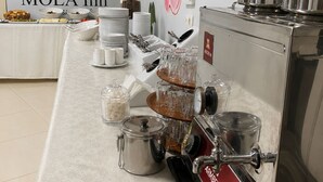 A buffet setup with various food items, a coffee machine, and a MOLA Inn sign in the background.