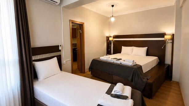 A hotel room with two beds, a bedside table, a lamp, and a ceiling light.