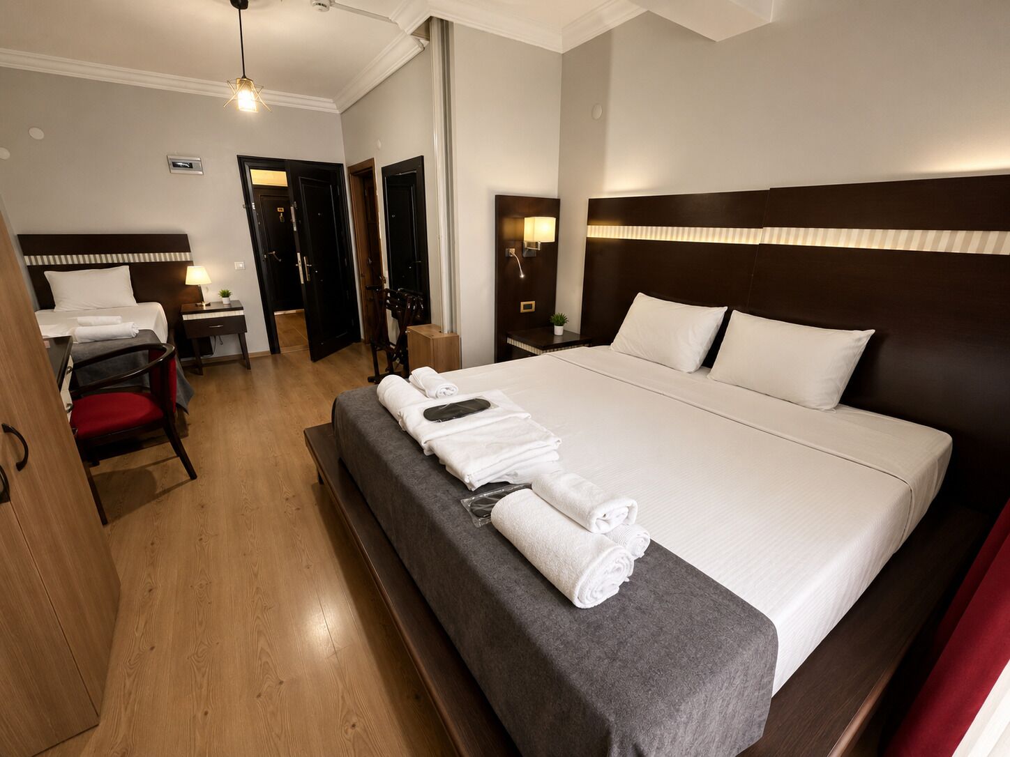 A hotel room with a large bed, bedside tables, a desk with a chair, and a red chair.