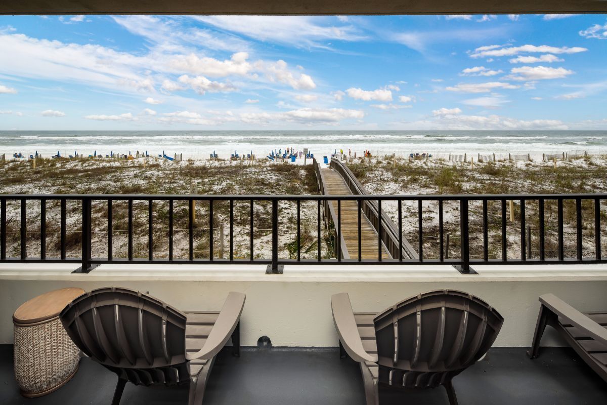 A balcony with a view of the beach, featuring a wooden deck and metal railing.
