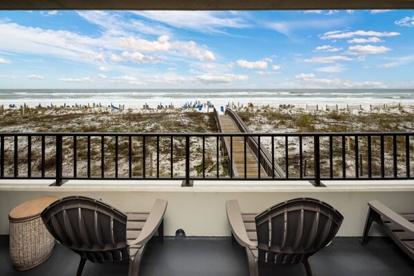 A balcony with a view of the beach, featuring a wooden deck and metal railing.