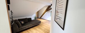 Loft moderno con un divano grigio scuro, pavimento in legno, soffitto a sbalzo e un’opera d’arte a parete raffigurante diversi attrezzi.