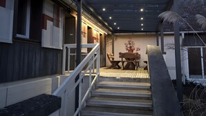 Un patio couvert avec un escalier menant à une terrasse en bois, une table avec des chaises et une plante en pot.