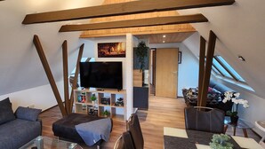 Un espace de vie moderne de style loft, doté d’un plafond haut, de poutres apparentes, d’un téléviseur à écran plat, d’un canapé, d’une table basse et d’un coin repas.
