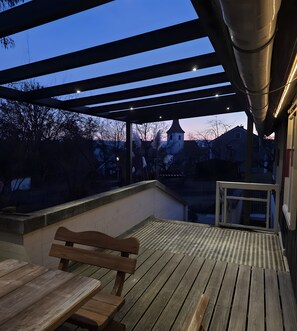 Una terraza exterior con un banco de madera y una estructura de pérgola.