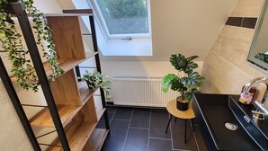 Une salle de bain moderne avec un puits de lumière, un radiateur, un lavabo et une plante en pot.