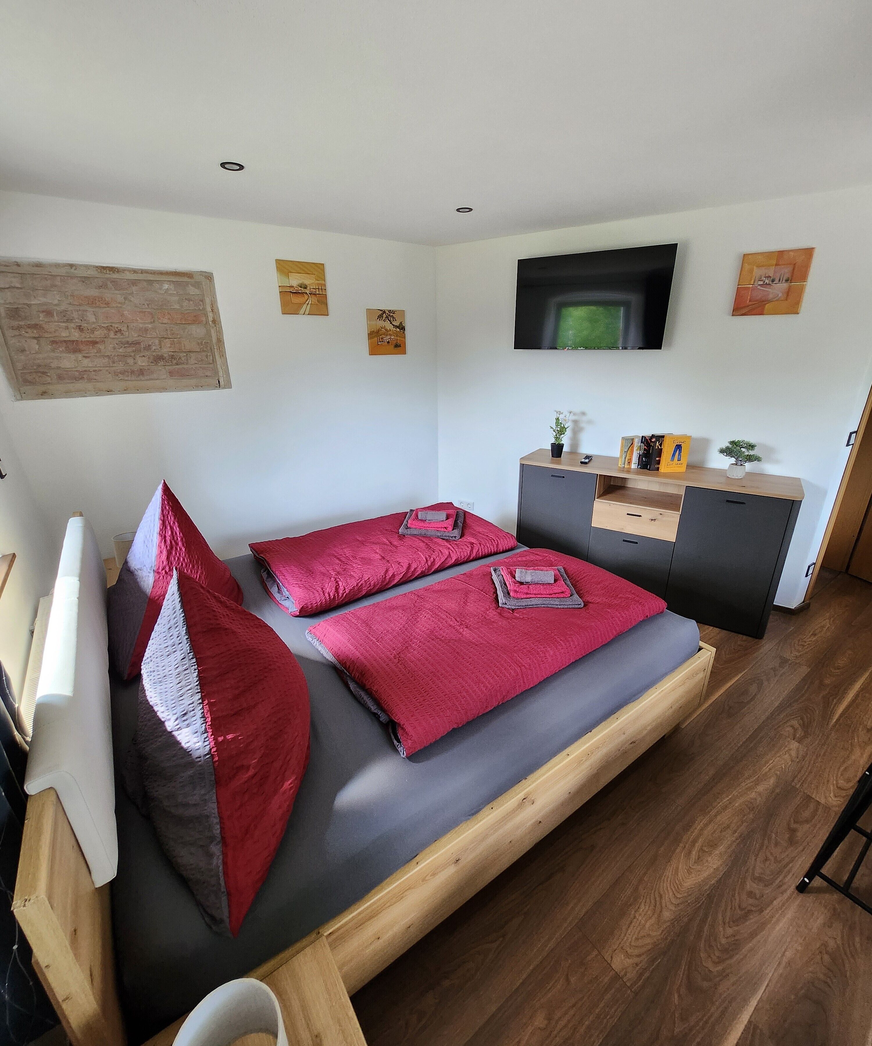 Ein Schlafzimmer mit einem Bett, einem Fernseher, einem Schreibtisch und einer kleinen Pflanze.